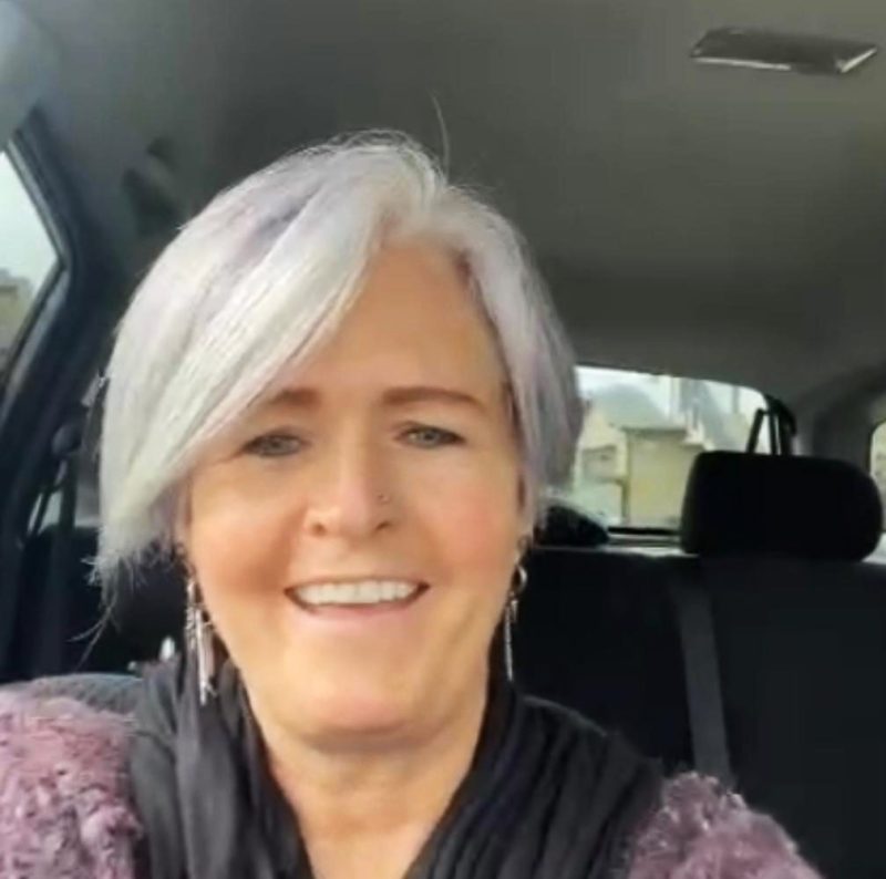 A woman with white hair sitting in the back of a car.